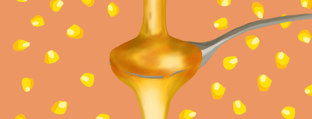Corn kernels surround flowing high fructose corn syrup on a silver spoon.