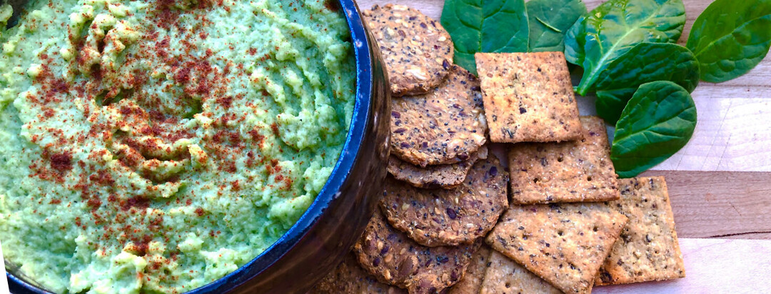 Spinach artichoke dip on a plate with a variety of crackers
