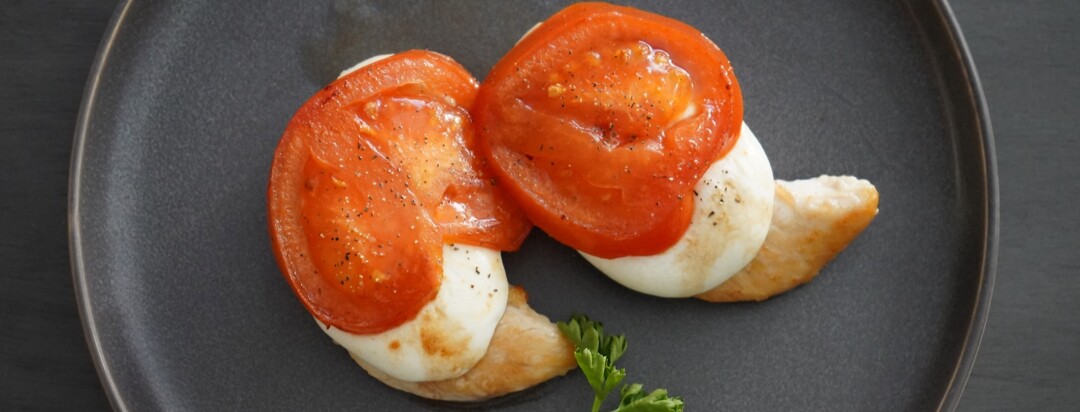 Two chicken breasts on a white plate with tomato and mozzarella.