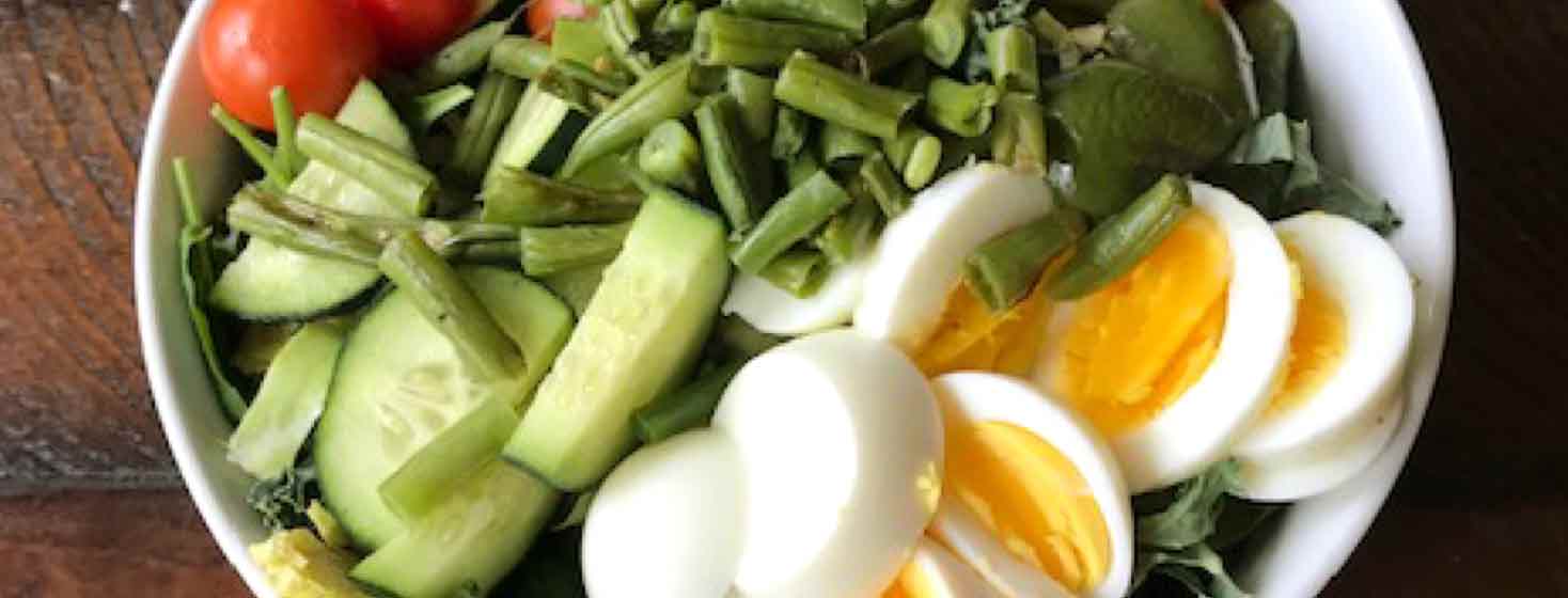 Salad bowl with chopped hard boiled egg, tomato. green beans and cucumbers.
