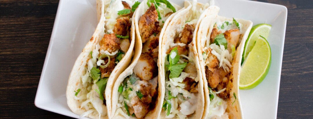 Fish tacos with cilantro coleslaw on a whit plate garnished with lime