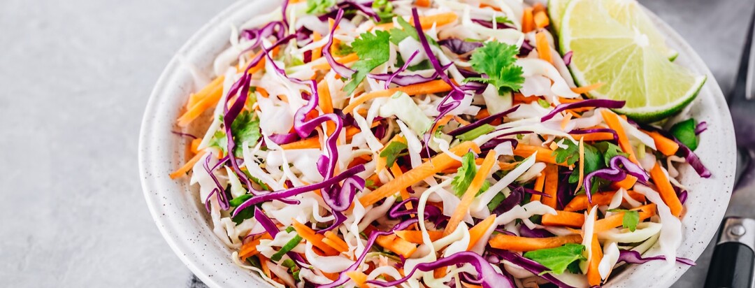 Cilantro coleslaw in a white bowl garnished with lime