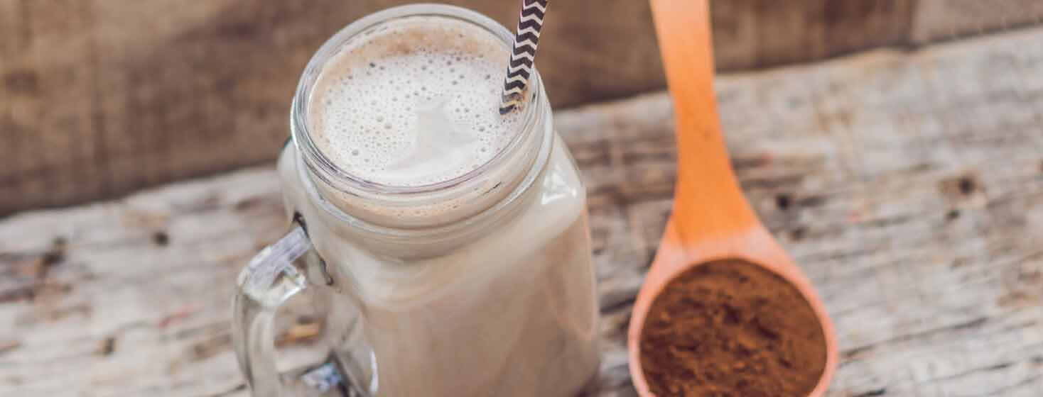 Chocolate smoothie in a mason jar next to a spoonful of cocoa
