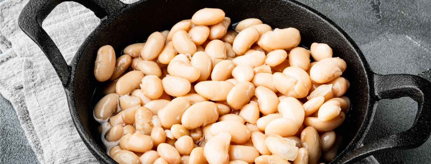 Iron skillet full of cooked cannellini beans on a tablecloth
